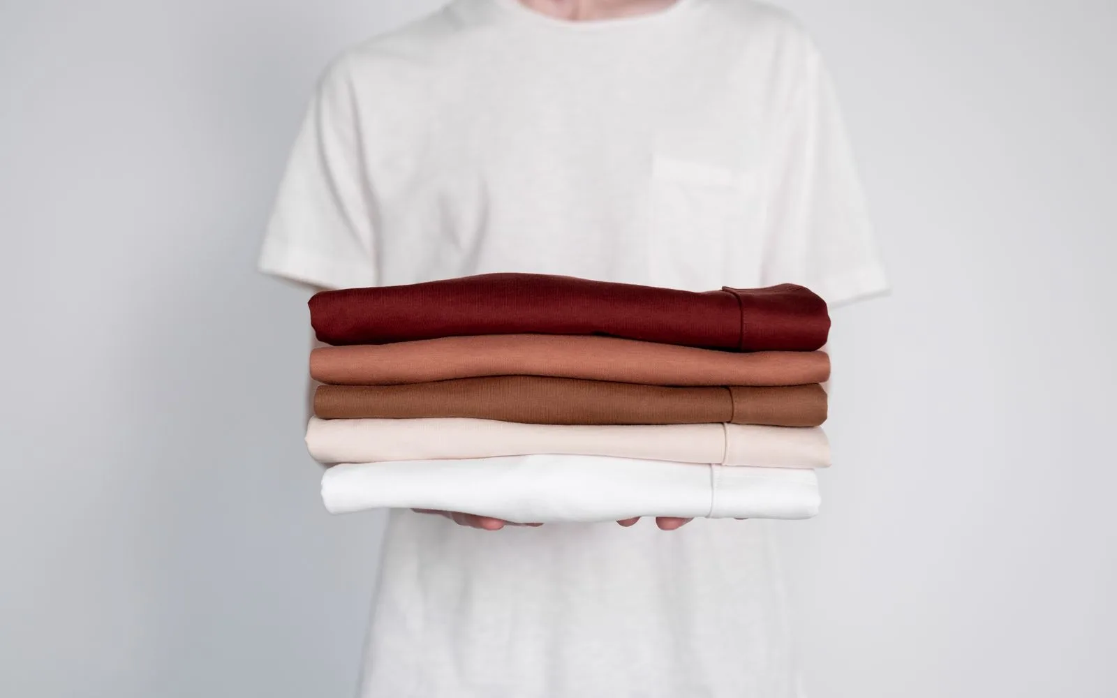 Person holding a tidy stack of neutral-coloured shirts