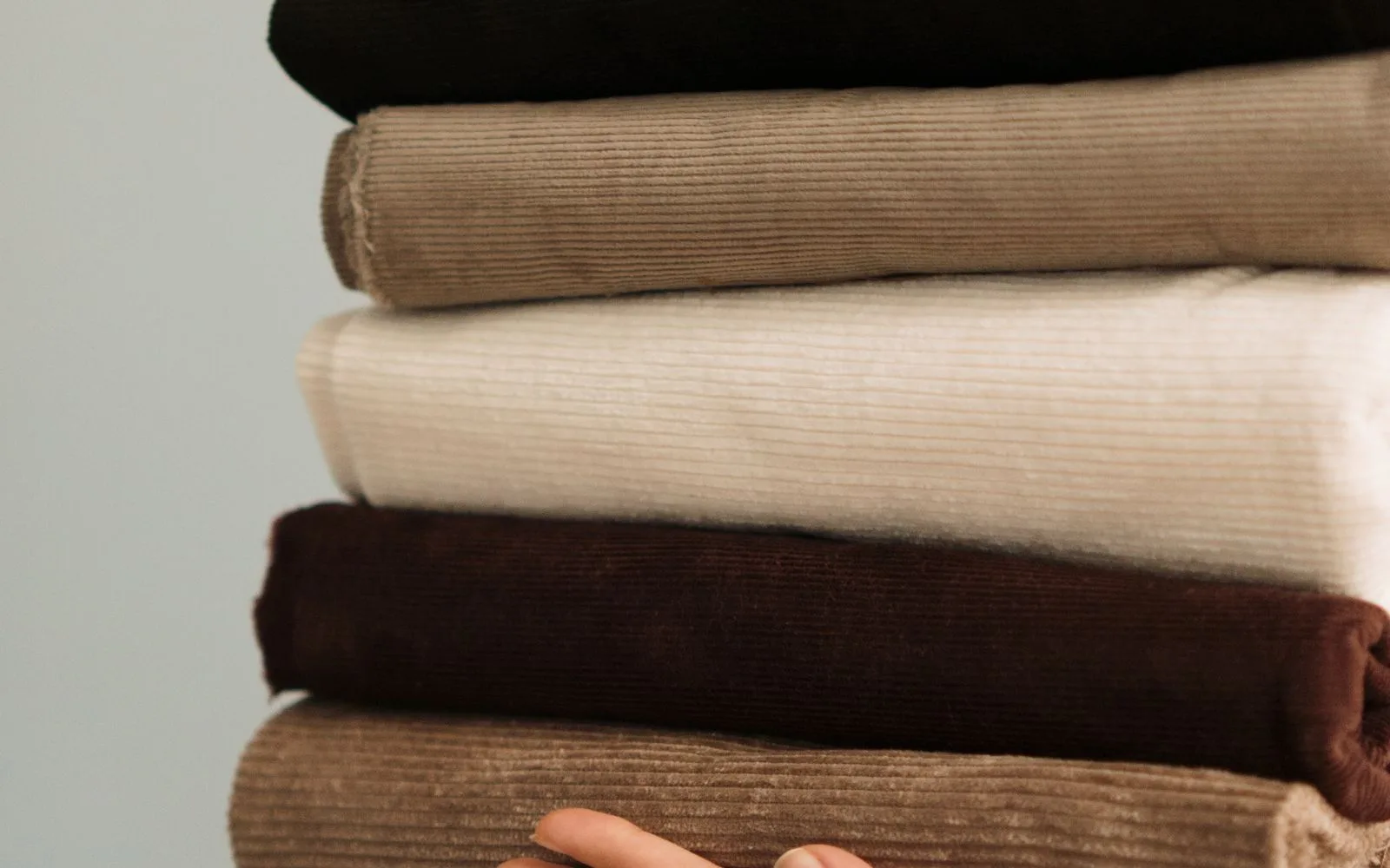 Person holding a coordinated stack of folded fabrics in neutral tones